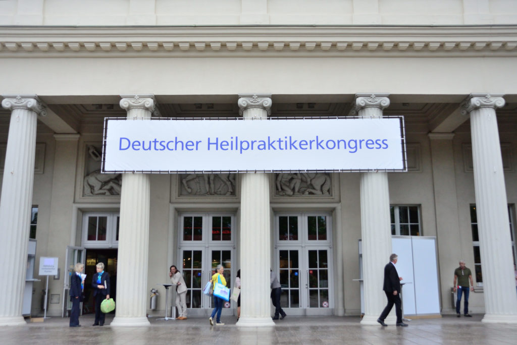 Großer Eingangsbereich eines alten Gebäudes mit vielen großen Säulen. Über drei Säulen hängt ein Banner mit der Aufschrift "Deutscher Heilpraktikerkongress"