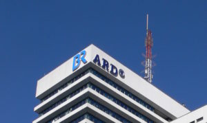 Der oberste Teil eines Hochhauses von unten fotografiert. Ein großer Antennemast darauf sowie in sehr groß die Logos des BR (Bayerischer Rundfunk) sowie der ARD.