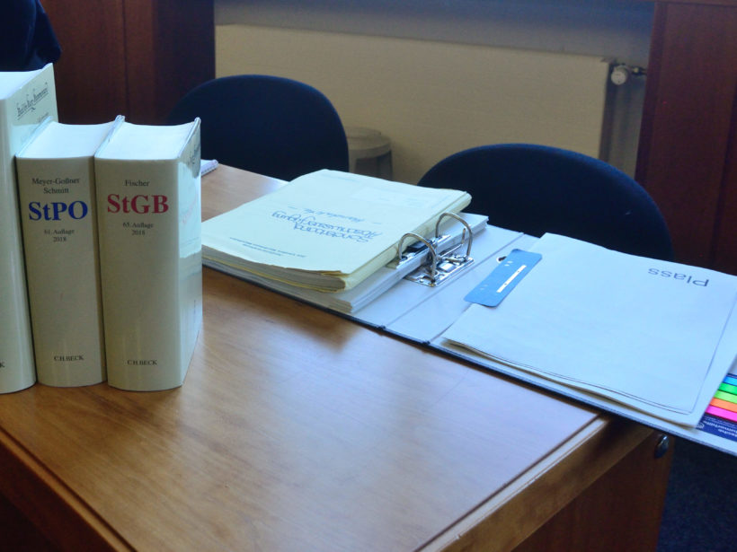 Schreibtisch mit einem geöffneten Ordner. Stehend drei dicke Bände des StGB (Strafgesetzbuch).