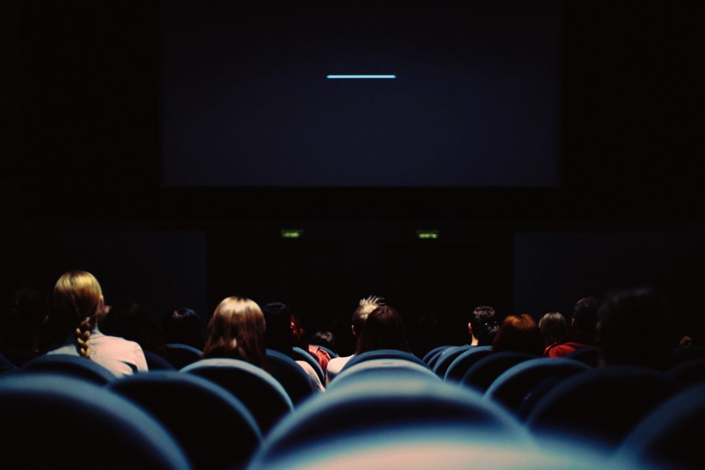 Blick von ganz hinten in die vorderen Reihen eines Kinosaals. Dunkler Hintergrund, dunkle Stühle, Menschen nur schemenhaft zu erkennen.