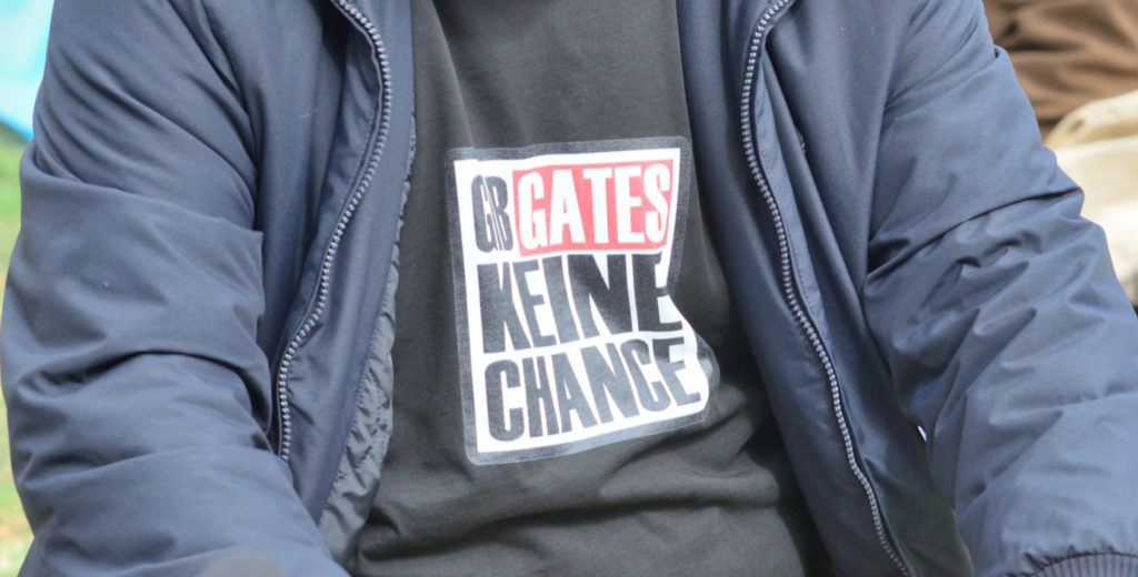 Person in Nahaufnahme, nur sein Shirt ist zu sehen auf dem der Spruch: "Gibt Gates keine Chance" steht. Die Wahl der Schrift und der Farben erinnert an die Überschriften der Bild-Zeitung.