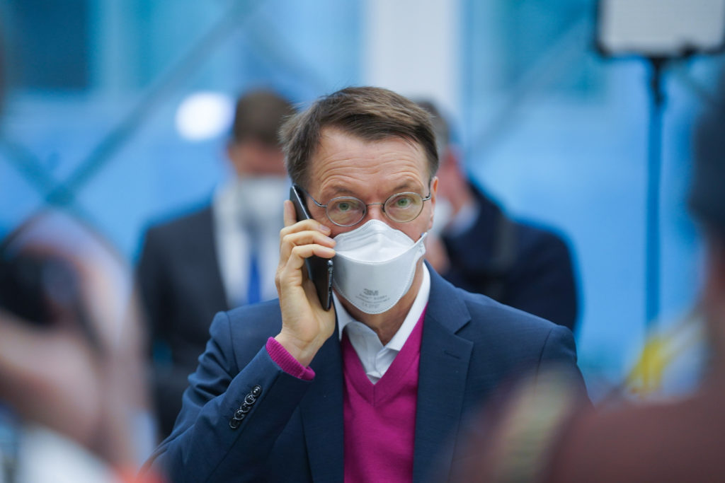 Mann mit Brille und FFP2-Maske vor Mund und Nase hält sich ein Handy ans Ohr.