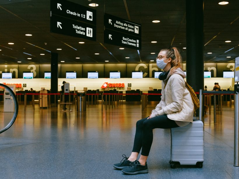 Frau mit Corona-Maske sitzt am Flughafen.