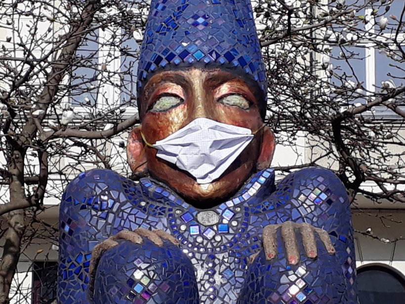 Skluptur eines Menschen mit Mosaik verziert. Diese trägt eine echte medizinische Maske.